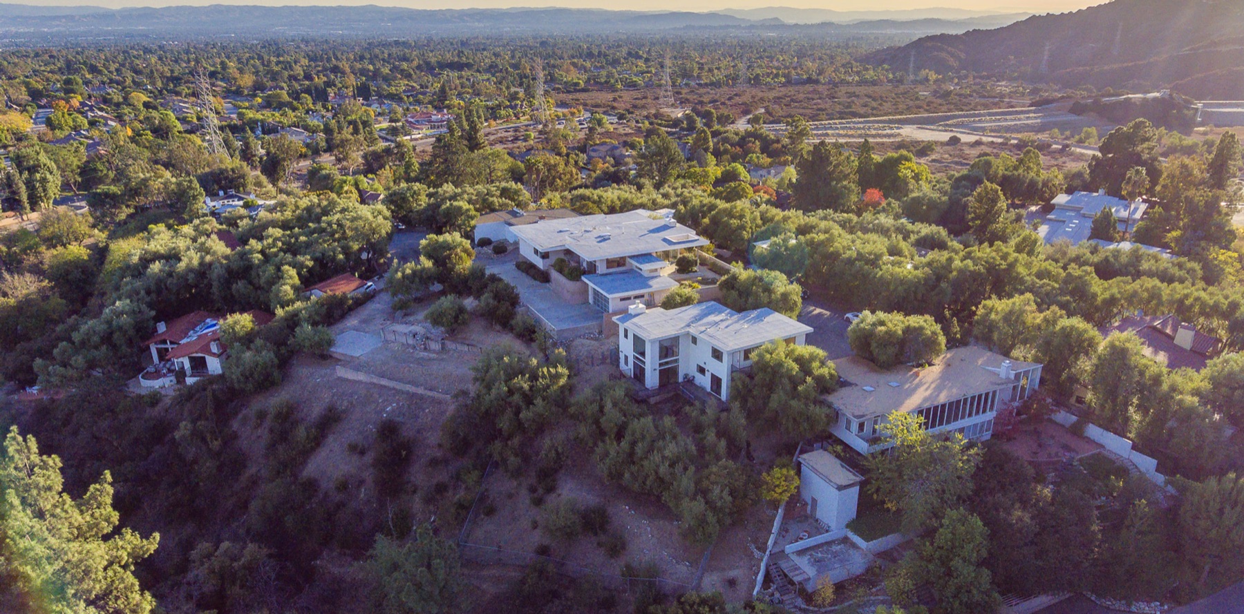Aerial view of a hillside estate compound overlooking a wide California valley at sunset