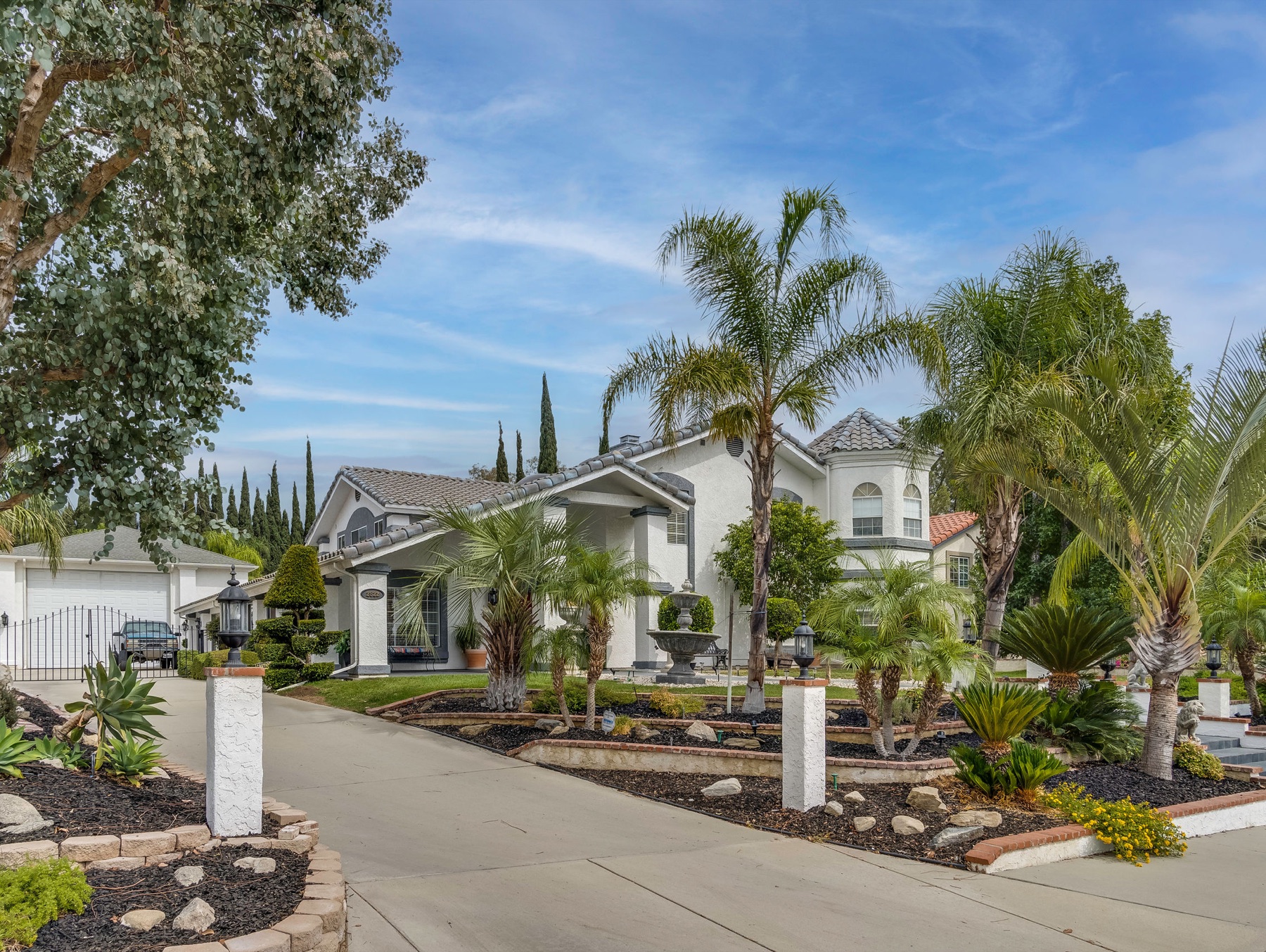 Front exterior of a High Desert home with palms, tile roof, and a stone fountain under clear sky